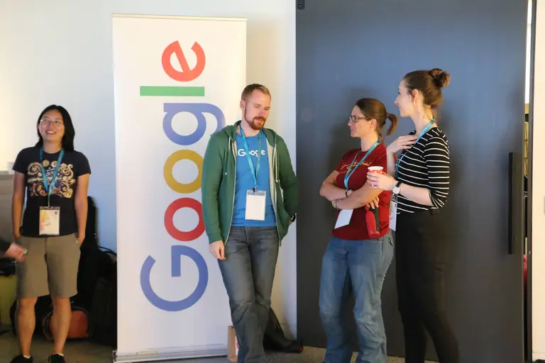 She Sharp attendees chatting together in front of a large Google logo wall at an evening event.